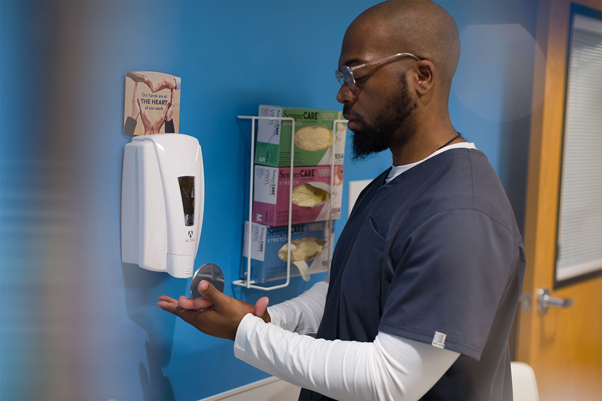 Man using an Altra Hand Sanitizer Dispenser in Healthcare Hallway