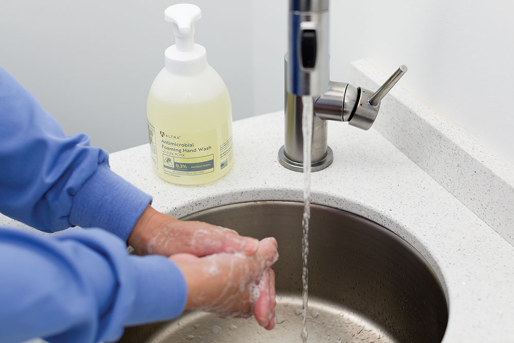 Altra Antimicrobial Foaming Hand Wash 550ml pump sitting by sink with medical professional washing hands