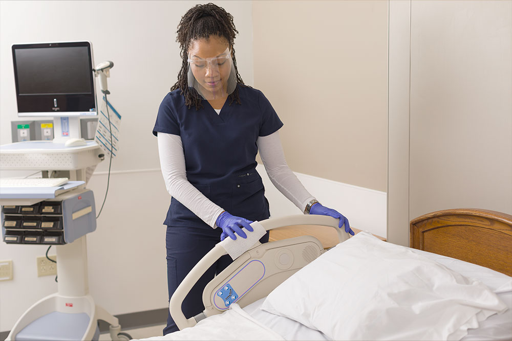 Woman wiping down hospital bed frame with an Altra One Disinfecting wipe.